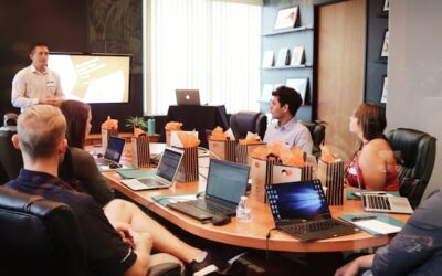 Schulungen für Mitarbeitende sind eine langfristige Investition. Um wirkungsvoll zu sein, sie gut geplant und die Lernergebniosse nachgehalten werden. Menschen sitzen mit Laptops um einen Konferenztisch und bekommen von einem Trainer eine Schulung.